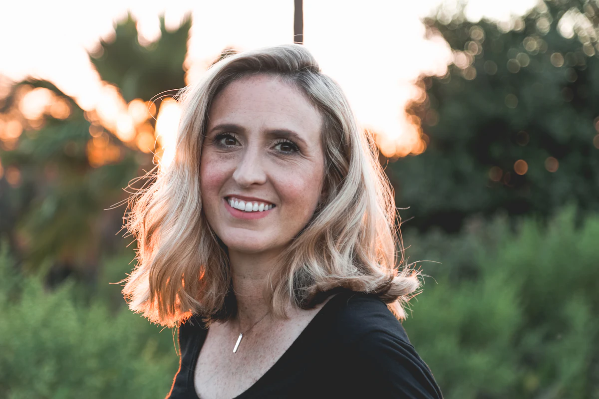 Žena kolem 40 s blond vlasy, klidný úsměv venku